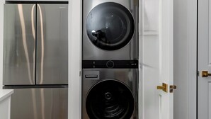 Una cocina compacta con refrigerador de acero inoxidable, lavadora y secadora integradas, y armarios blancos.