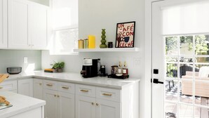 Una cocina con armarios blancos, una cafetera y ventana con vistas a un jardín.