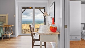 A room with a view through a glass door, a table with a vase, a chair, and a lamp.