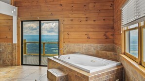 A bathroom with a large bathtub, wooden walls, and a view of the mountains through a glass door.
