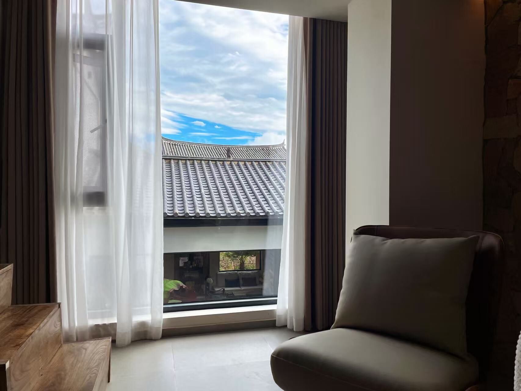Habitació amb una finestra gran, vista a un teulat tradicional i una cadira moderna.
