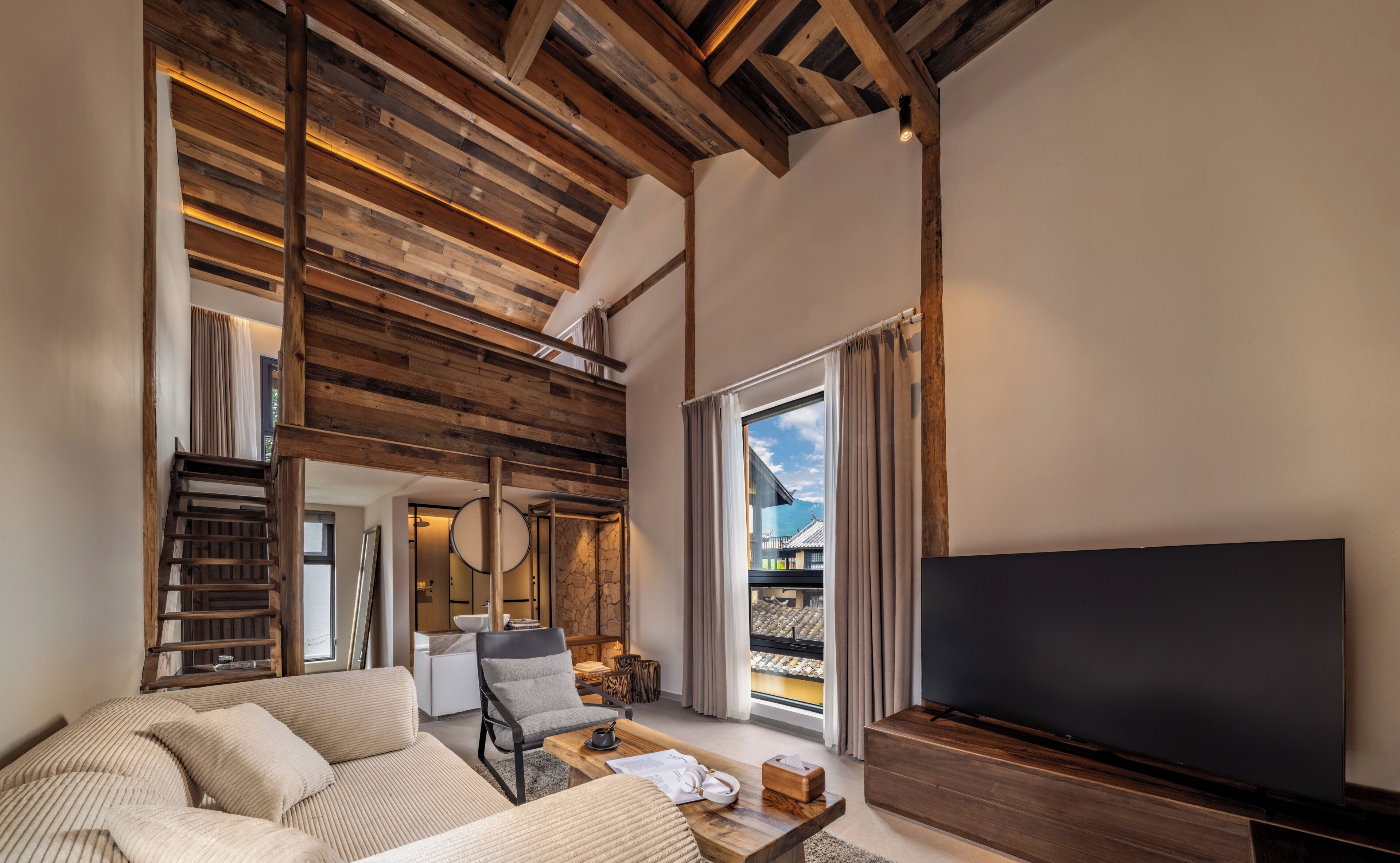 A modern living room with a large TV, wooden ceiling beams, a sofa, and a view of a traditional building outside.