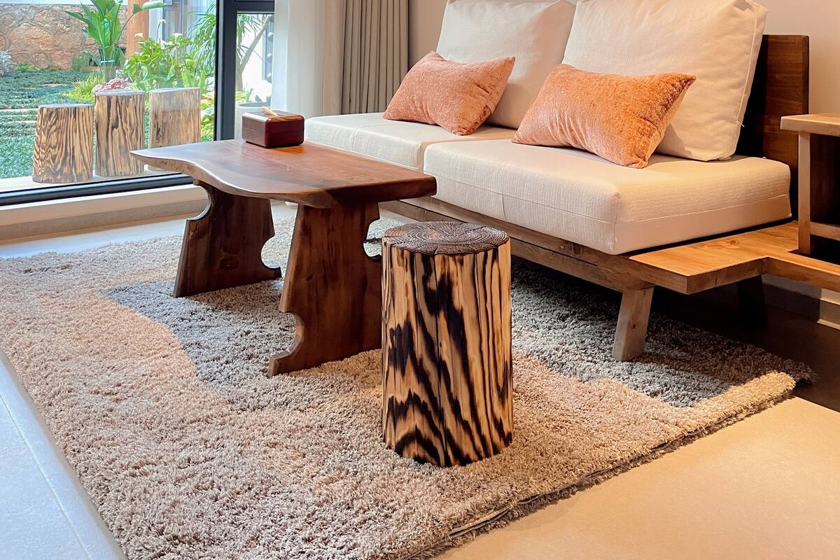 Een moderne woonkamer met een bank, salontafel en decoratieve kussens. Er hangen kunstwerken aan de muur en er is uitzicht op het landschap door grote ramen.