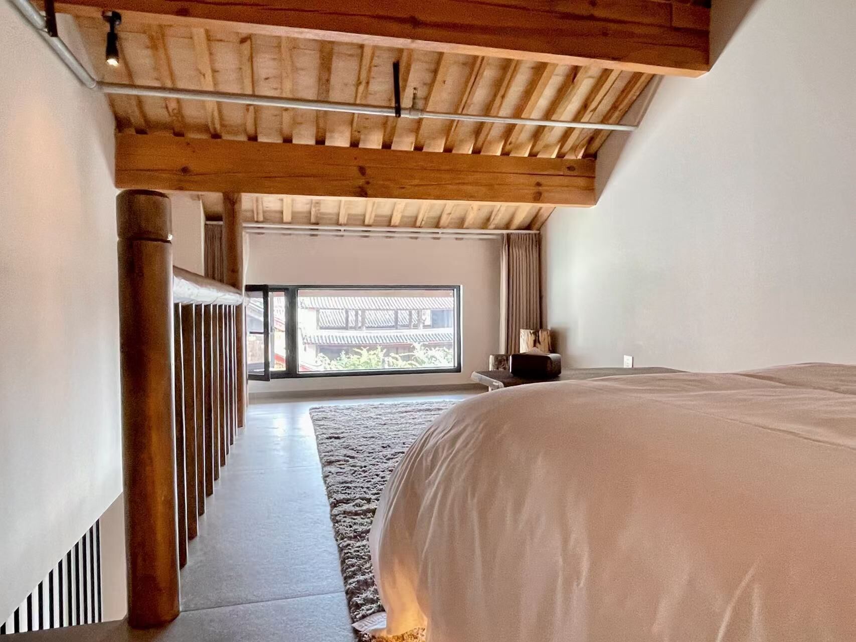 A bedroom with a large bed, a wooden ceiling, and a view of a traditional building through a glass door.