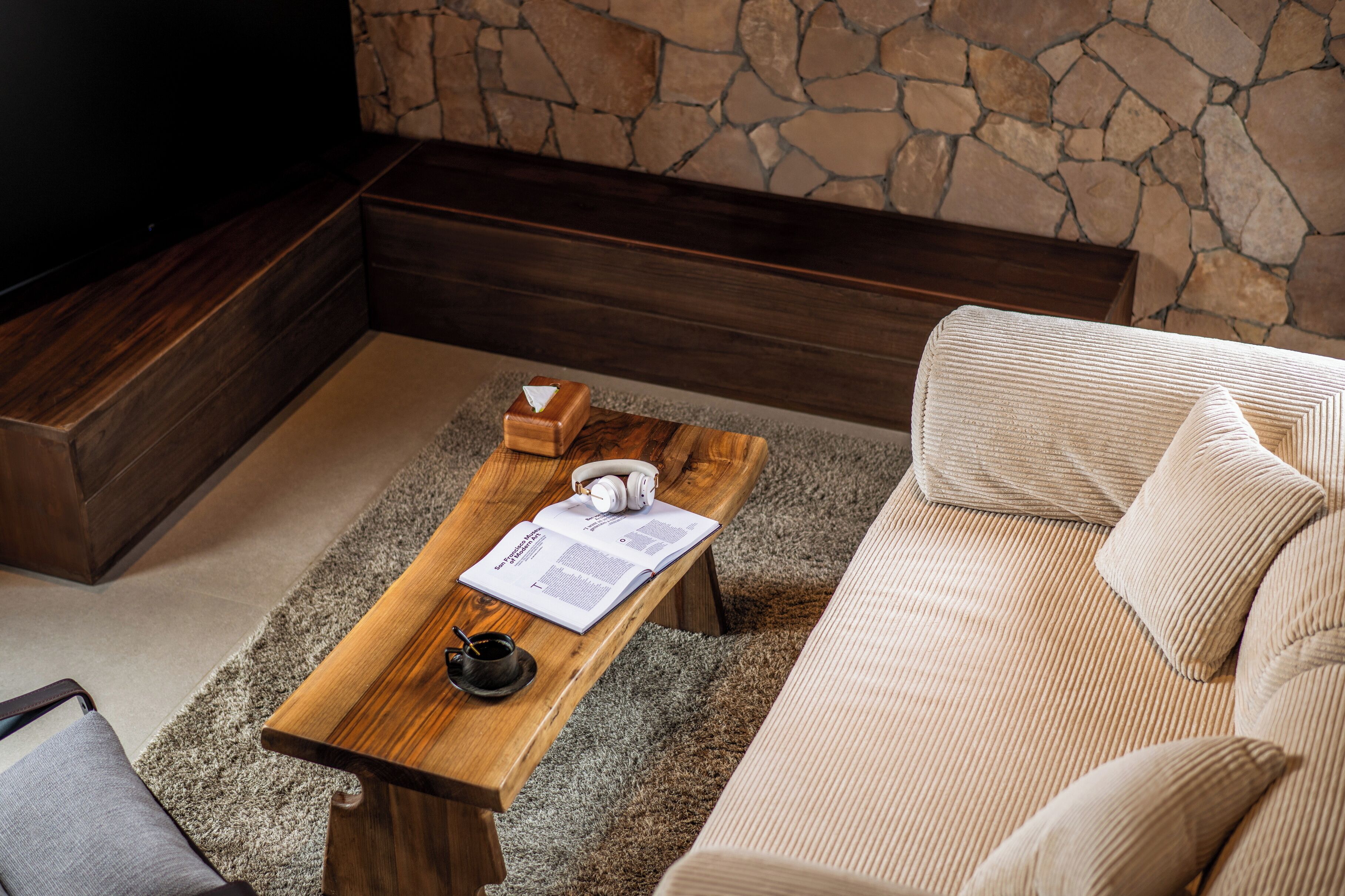 A cozy living area with a wooden coffee table, a beige sofa, and a stone wall.