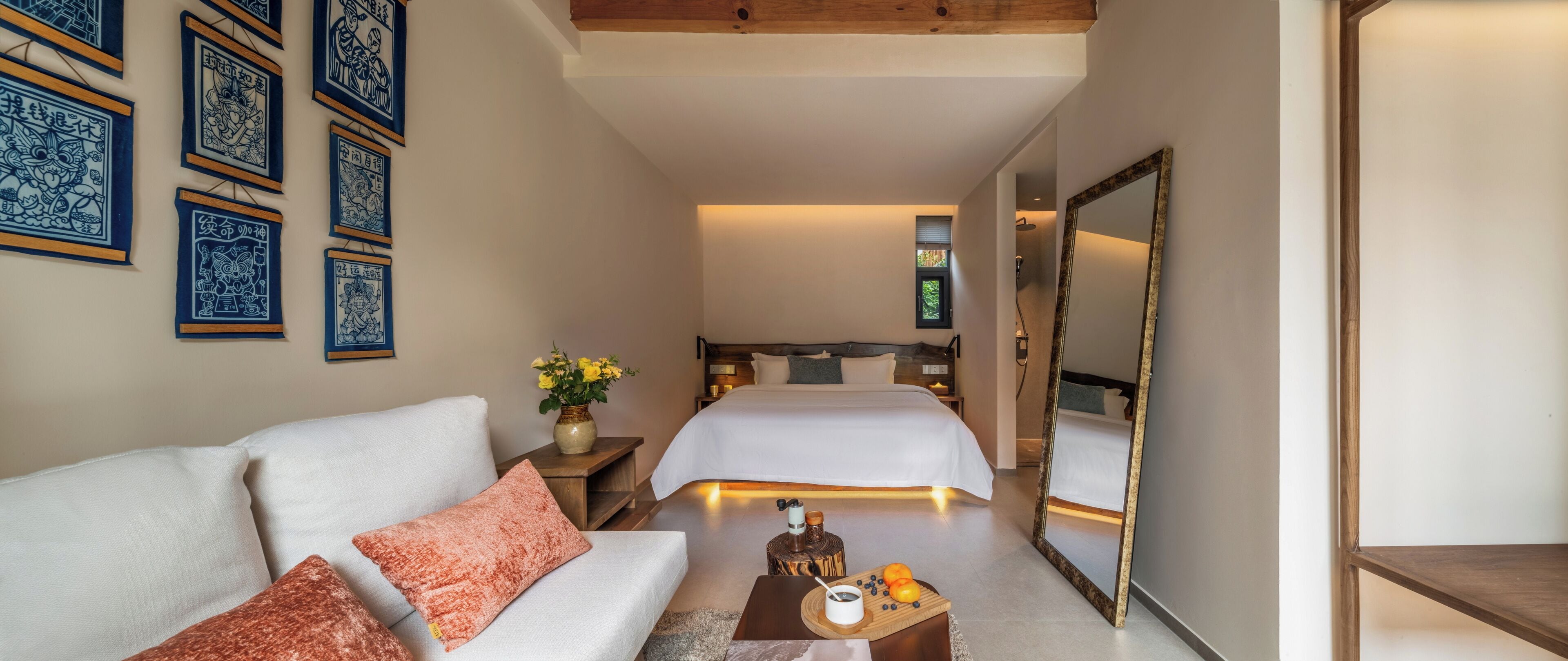 Ein Hotelzimmer mit einem großen Bett, einem Schlafsofa, einem kleinen Tisch mit Blumenvase und einem Spiegel.