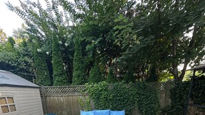 Un espace patio avec une maison grise, un ensemble de meubles de jardin en osier et un sol recouvert de gravier.