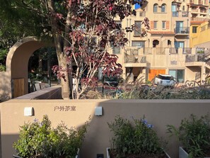 A residential building with balconies, a tree with red leaves, and a sign reading "户外茶室" (outdoor tea room). - Clouds on the Horizon (Dali)