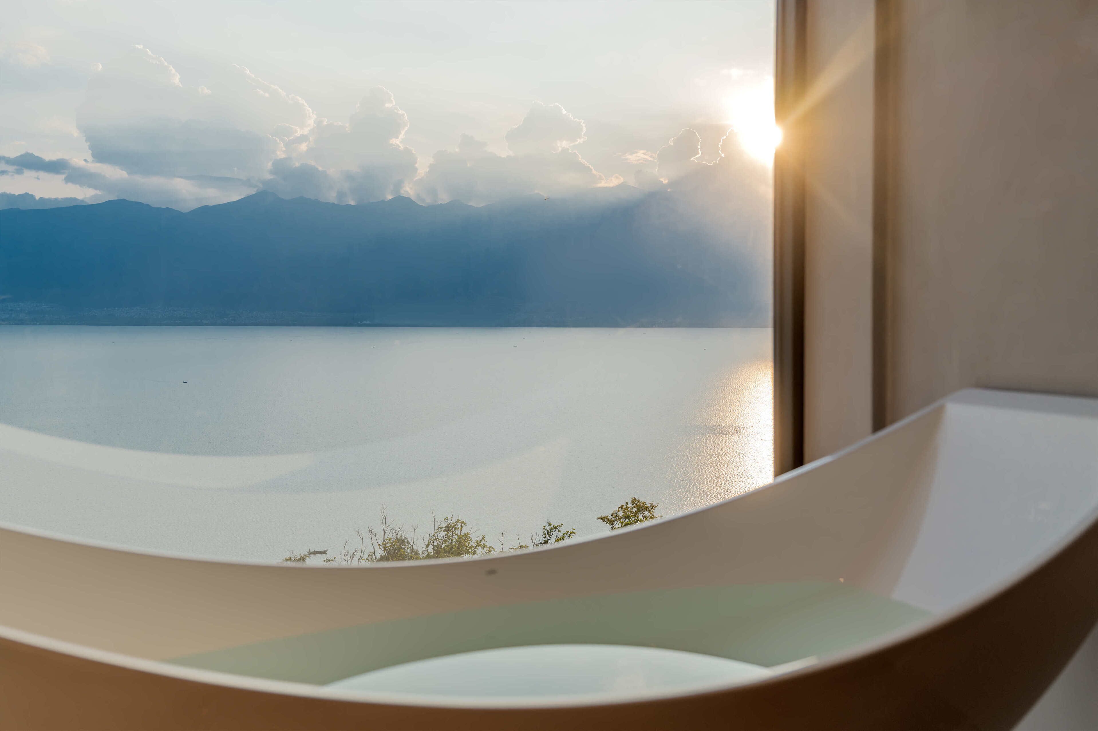 A bathtub with a view of a calm lake and mountains in the background.