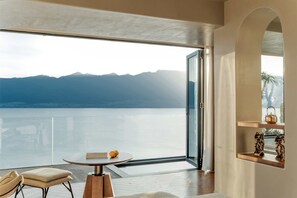 Une chambre moderne dotée d’une grande porte vitrée donnant sur un balcon avec vue sur un lac et des montagnes.