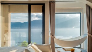 A bedroom with a large window, a hammock, and a view of the sea and mountains.