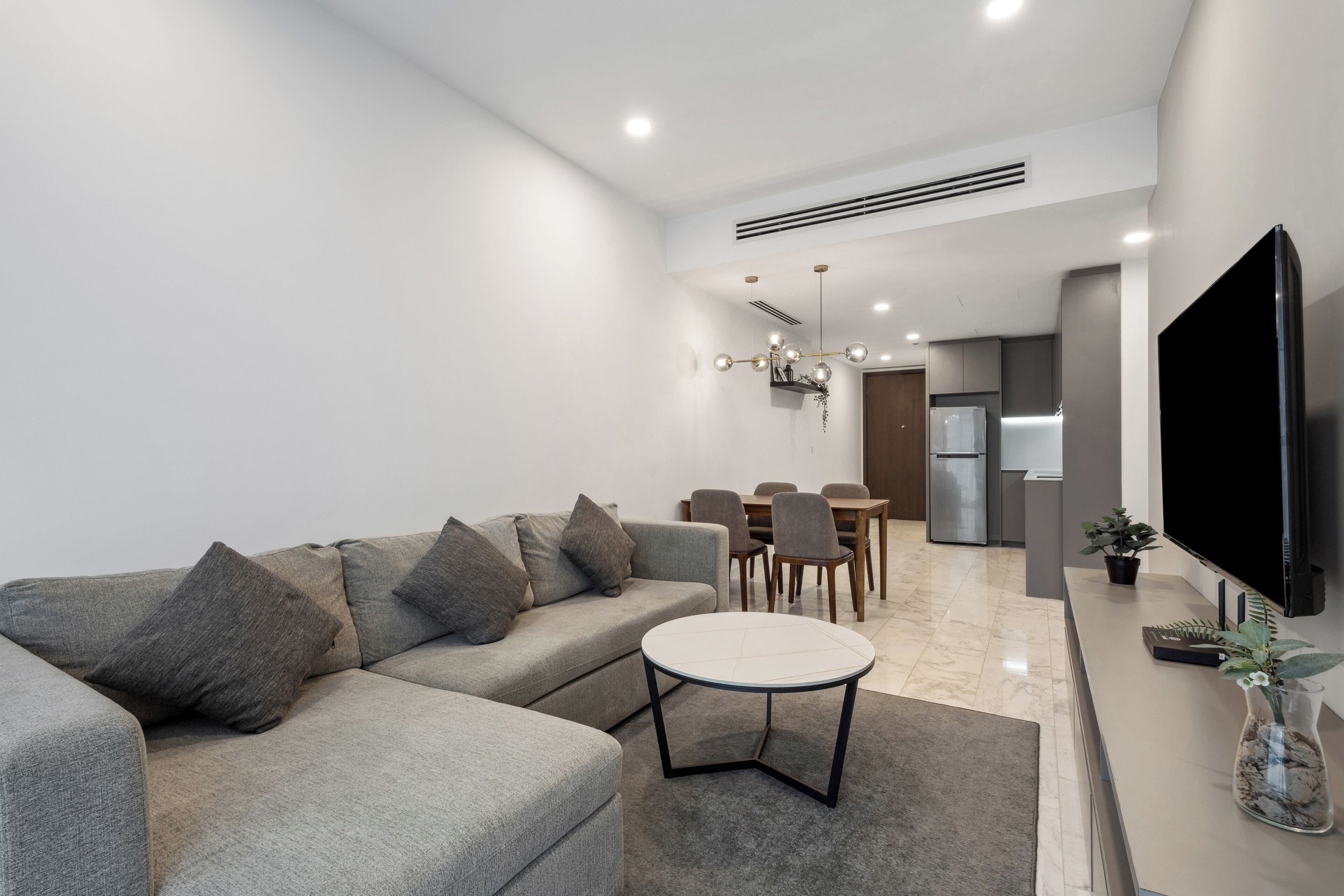 Ein modernes Wohnzimmer mit einem Ecksofa, einem runden Couchtisch und einem Flachbildfernseher.