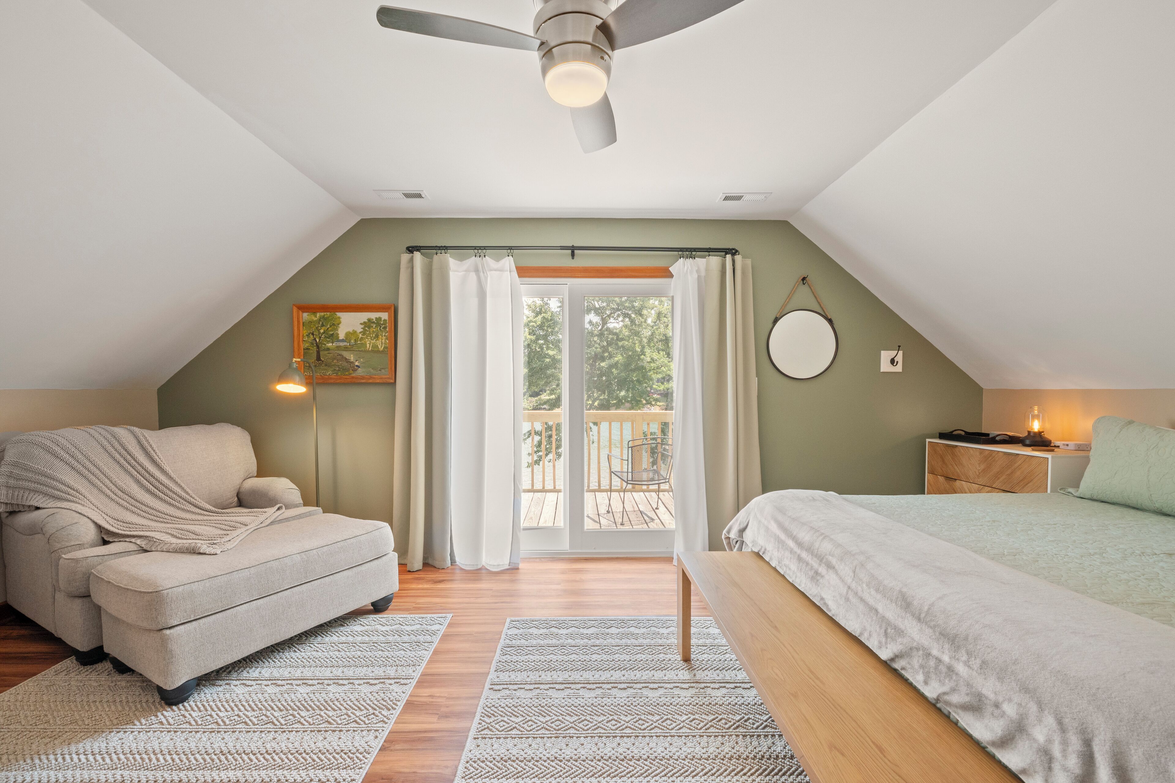 Une chambre confortable avec un lit, une chaise, un ventilateur de plafond et un balcon agrémenté de rideaux.