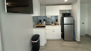 A compact kitchen with white cabinets, a stainless steel refrigerator, a microwave, and a TV mounted on the wall. - Bimini Beach Getaway #2 (Alice Town)