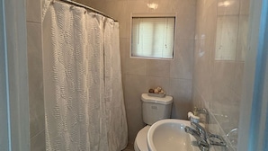 A small bathroom with a shower curtain, toilet, and sink. - Bimini Beach Getaway #2 (Alice Town)