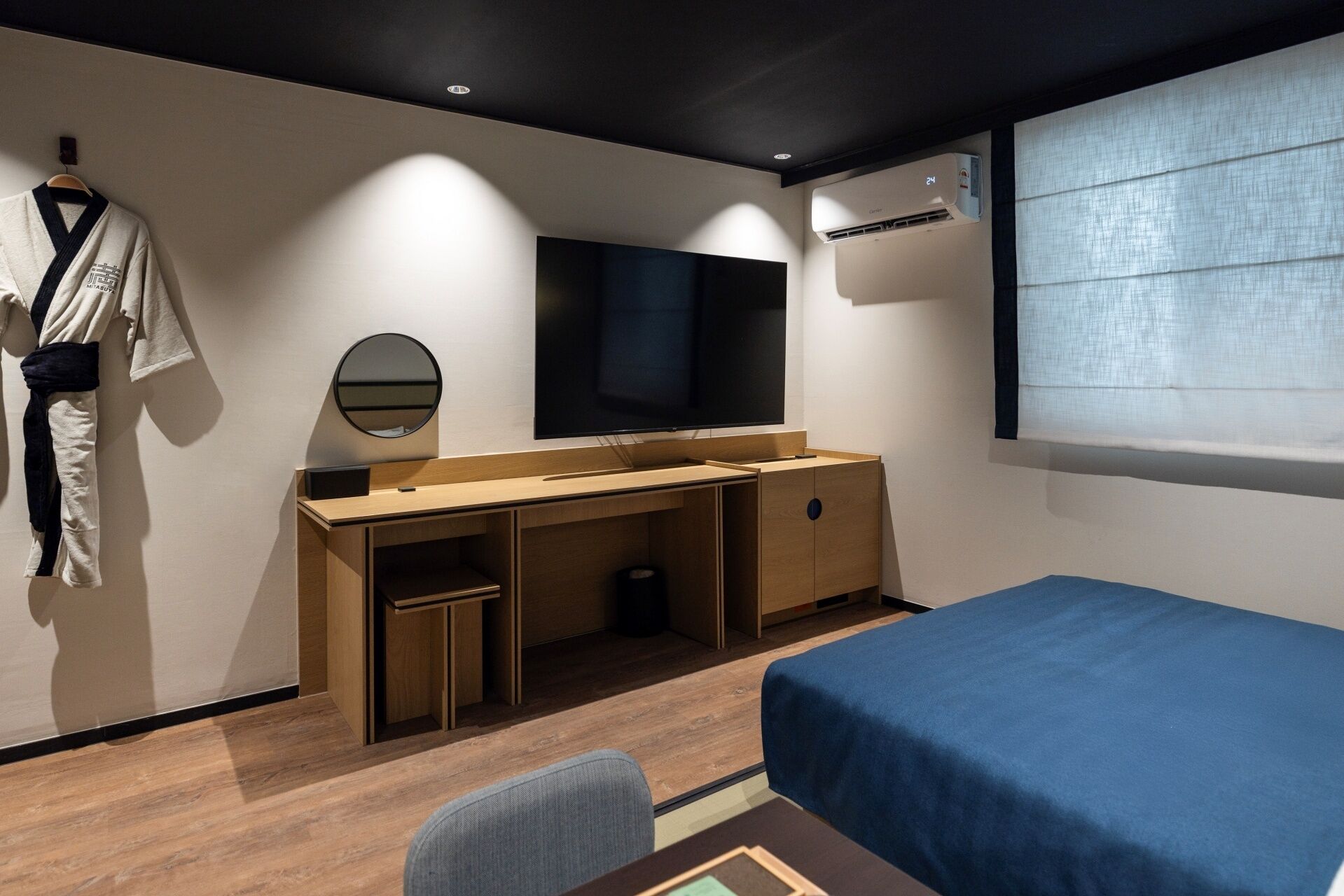 A modern bedroom with a wooden desk, a TV, a wardrobe, and a bed.