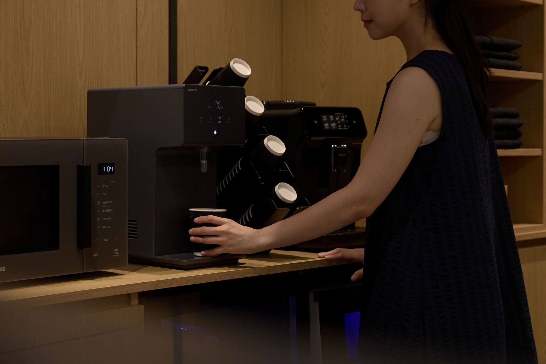 A person using a coffee machine with multiple cups and a microwave.