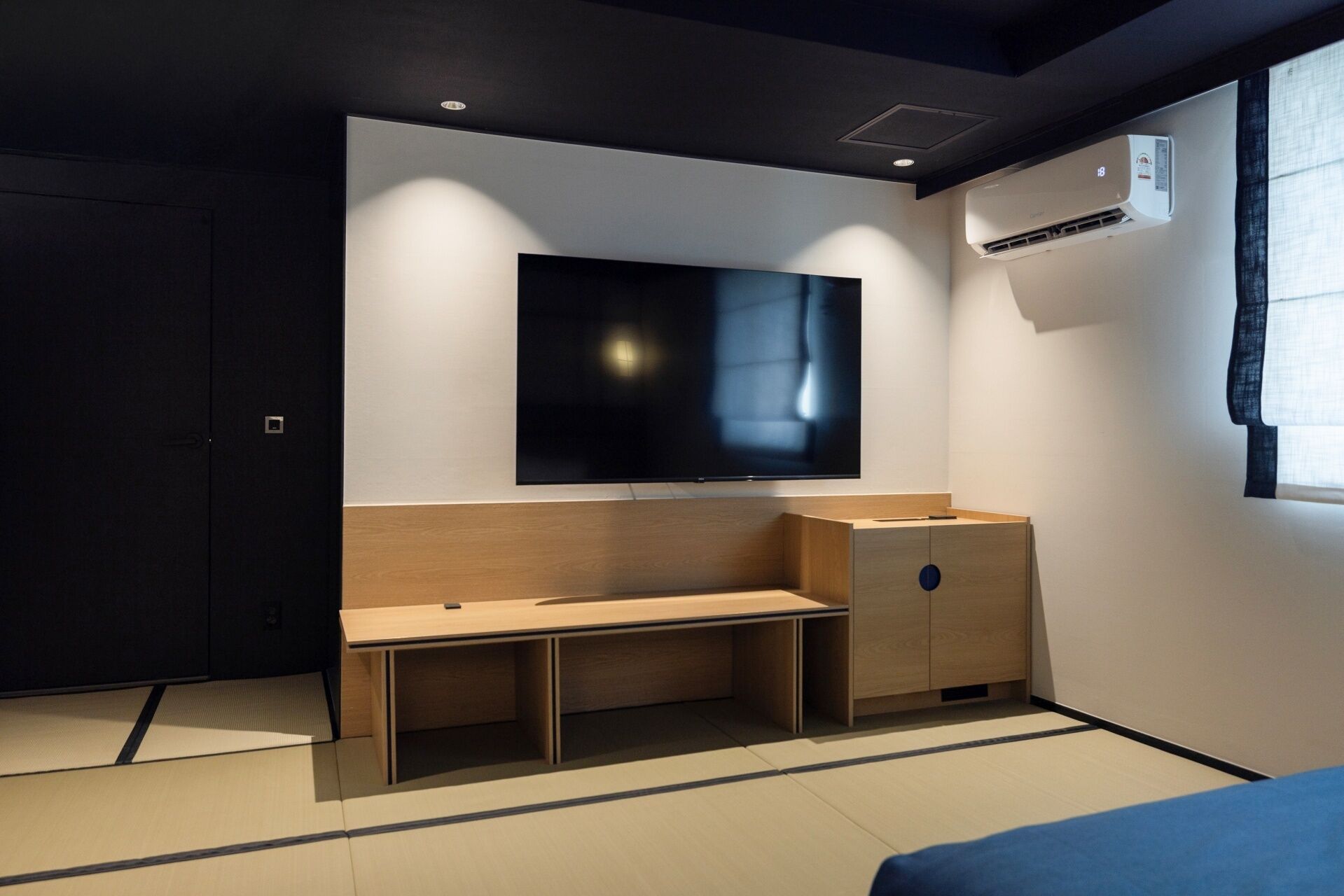 Quarto moderno com uma grande TV de tela plana na parede, um banco de madeira e um pequeno armário.