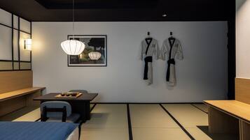 Ein modernes Zimmer mit Tatami-Böden, einem Holztisch, einer Pendelleuchte und zwei Kampfsport-Anzügen an der Wand.