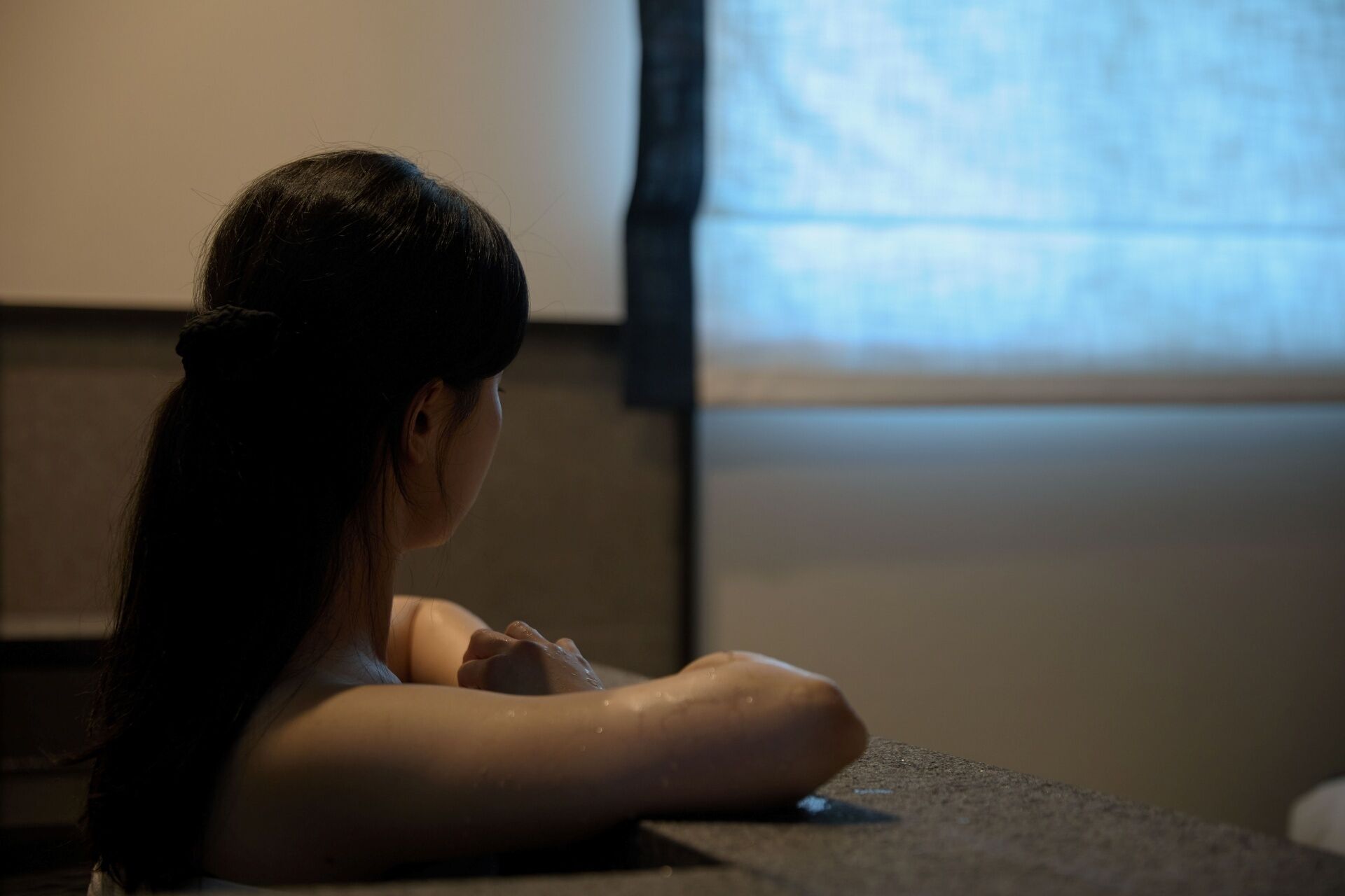 A person sitting in a dimly lit room with a window in the background.
