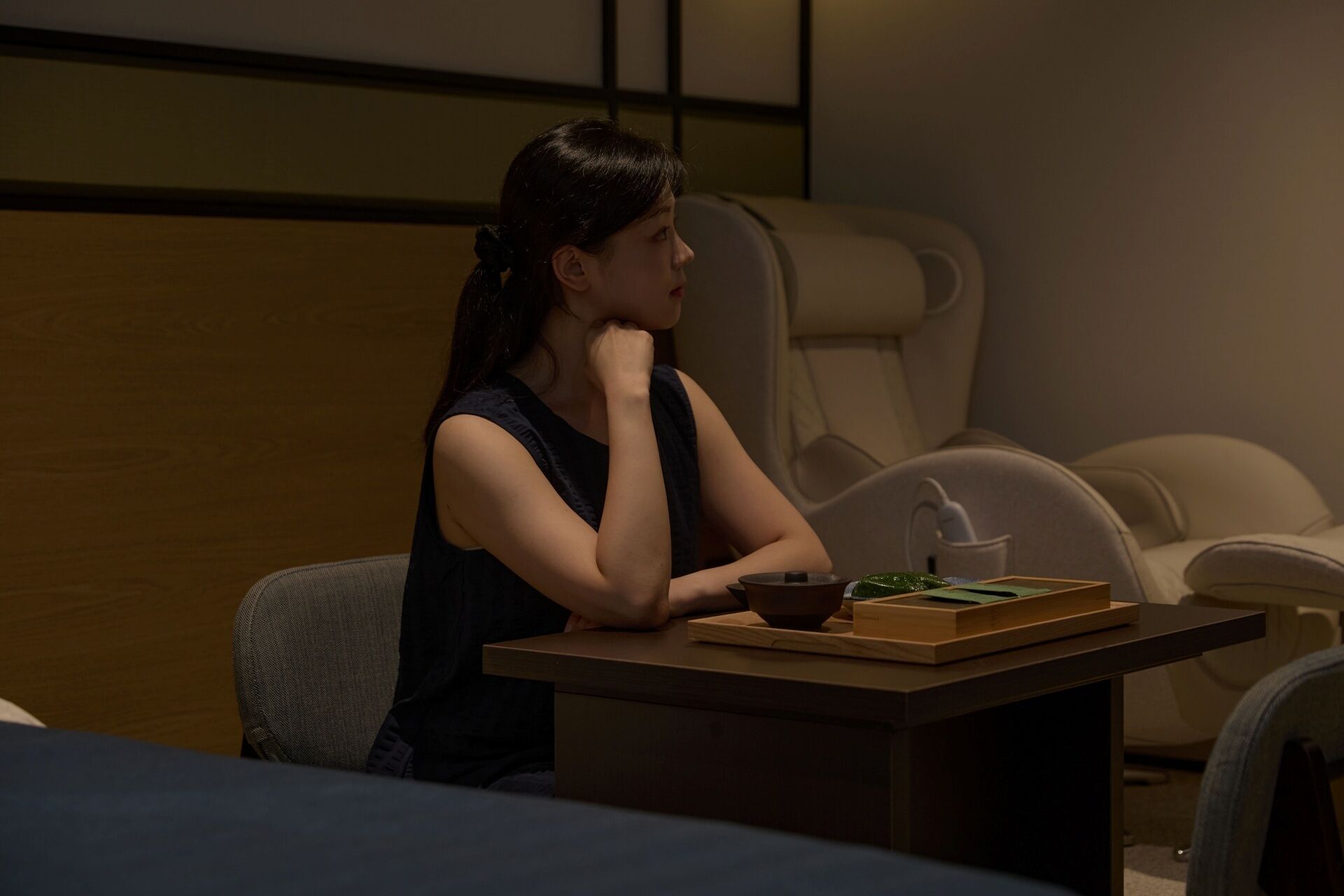 A person sitting at a table in a dimly lit room with a wooden panel wall and a cushioned chair.
