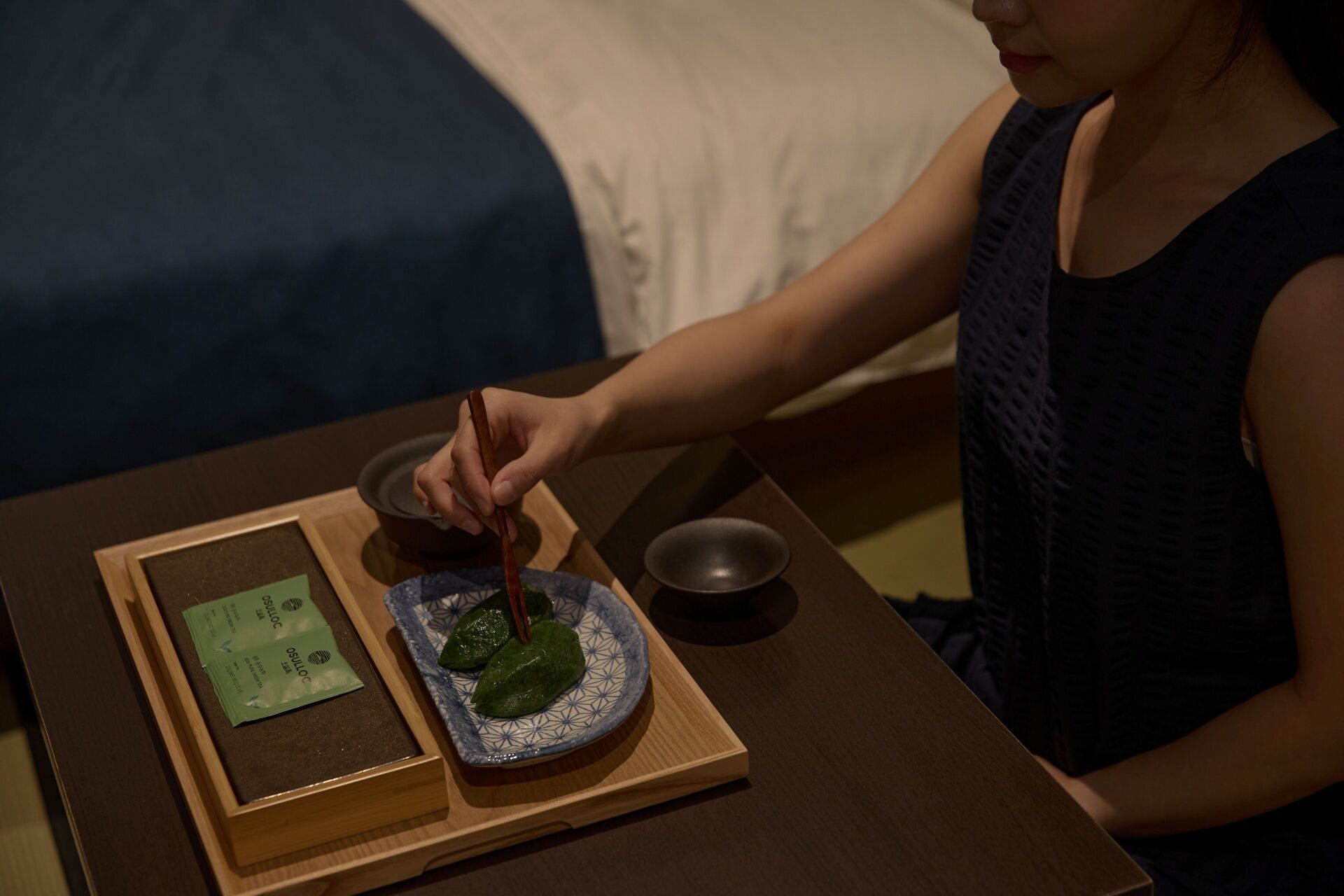A person preparing food on a wooden table with a plate, chopsticks, and a bowl.