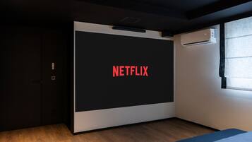 A modern room with a large screen displaying the Netflix logo, a dark door, and a window with blinds.