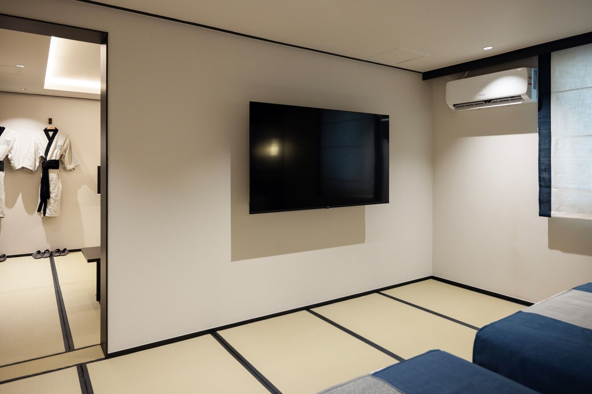 Una habitación de hotel moderna con suelo de tatami, televisor montado y aire acondicionado en el techo.