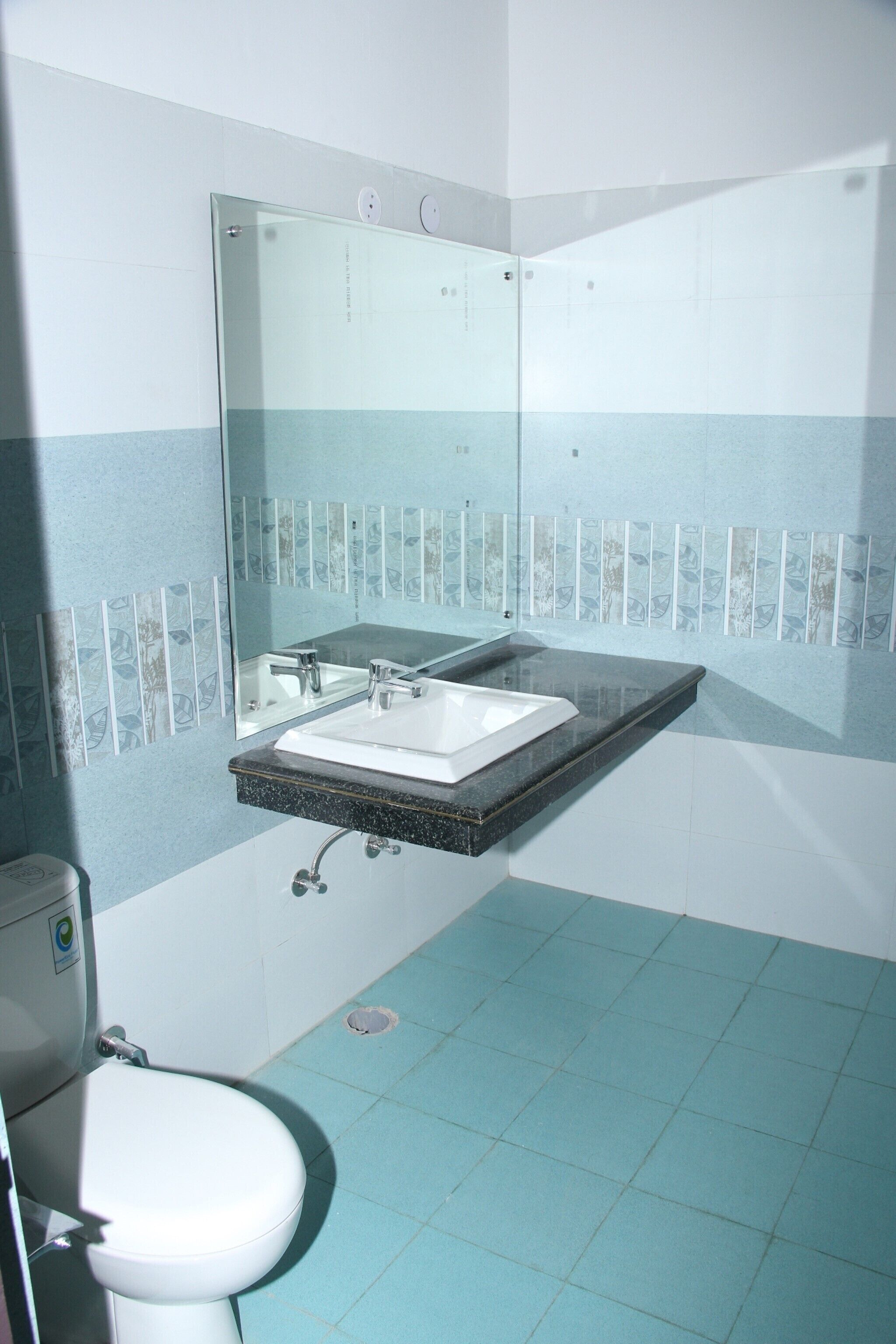 A bathroom with a white toilet, a sink with a mirror above it, and blue-tiled walls.