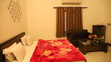 A hotel room with a bed, a sofa, a coffee table, and an air conditioner.