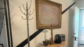 Una habitación con una mesa, perchero, un cuadro enmarcado y una puerta.