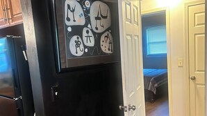 Una cocina con un refrigerador negro, una puerta blanca y una pared con arte abstracto.