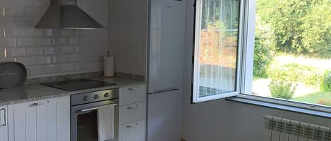 A kitchen with a stove, oven, refrigerator, and a window with a view of greenery.
