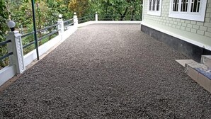 A covered outdoor area with a gravel floor, surrounded by a white railing and a building with white-framed windows. - Riverside Homestay by nature  (Mankulam)