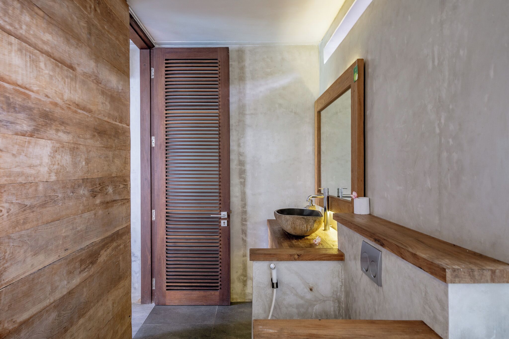 Ein Badezimmer mit Holztür, großem Spiegel und Waschtisch mit Waschbecken.
