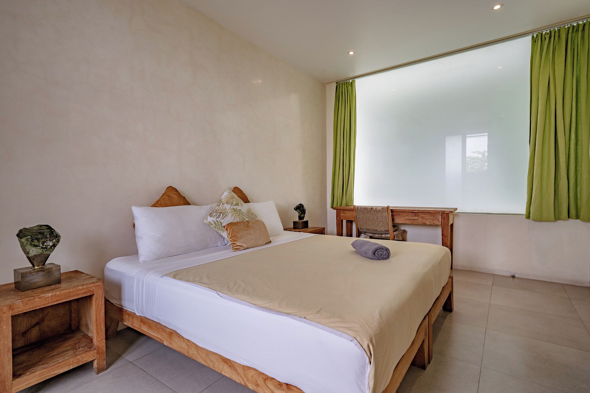 A bedroom with a large bed, a wooden nightstand, a small table, and a green curtain.