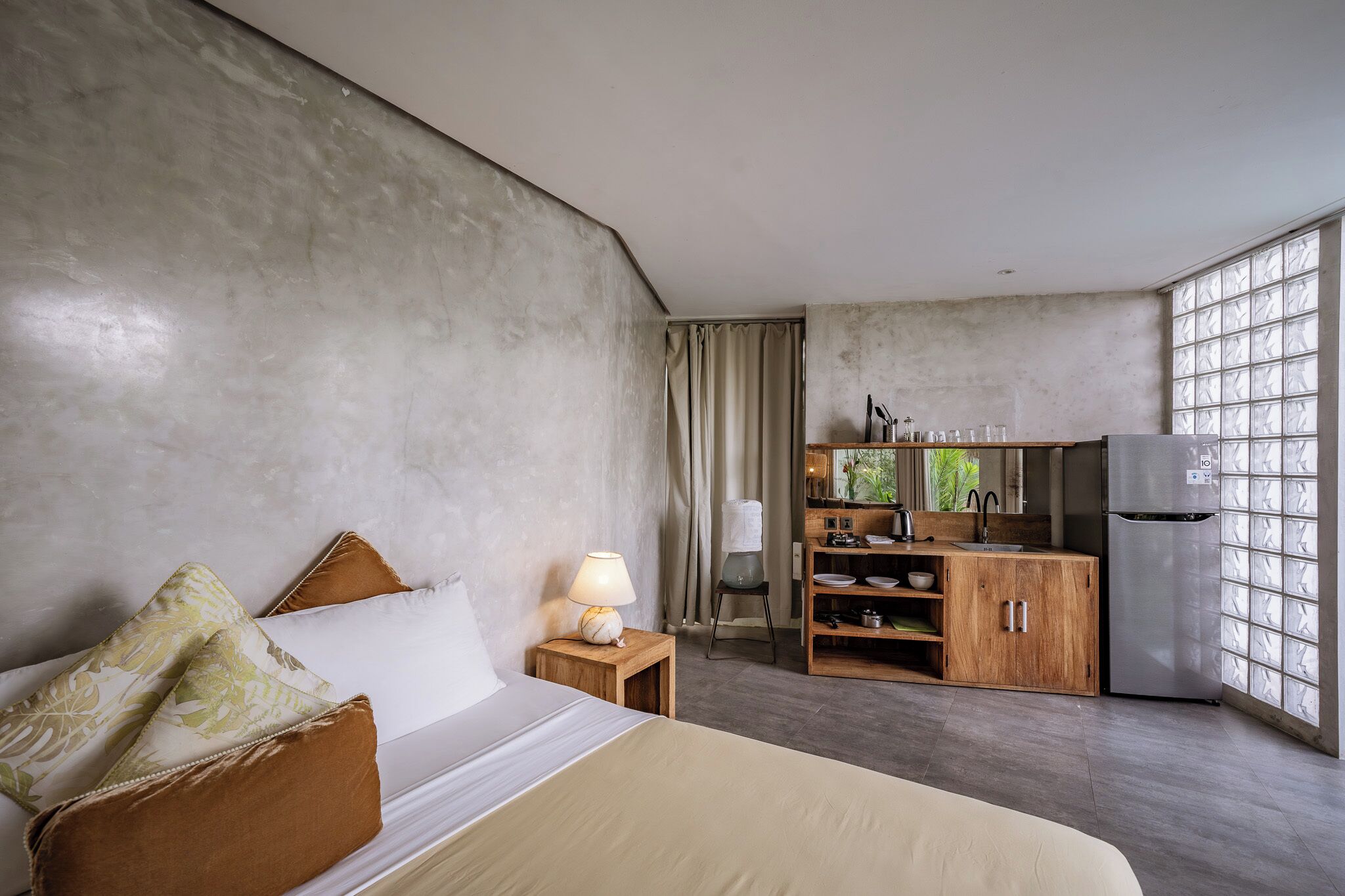 A bedroom with a bed, bedside table with a lamp, and a wooden cabinet with kitchen appliances.