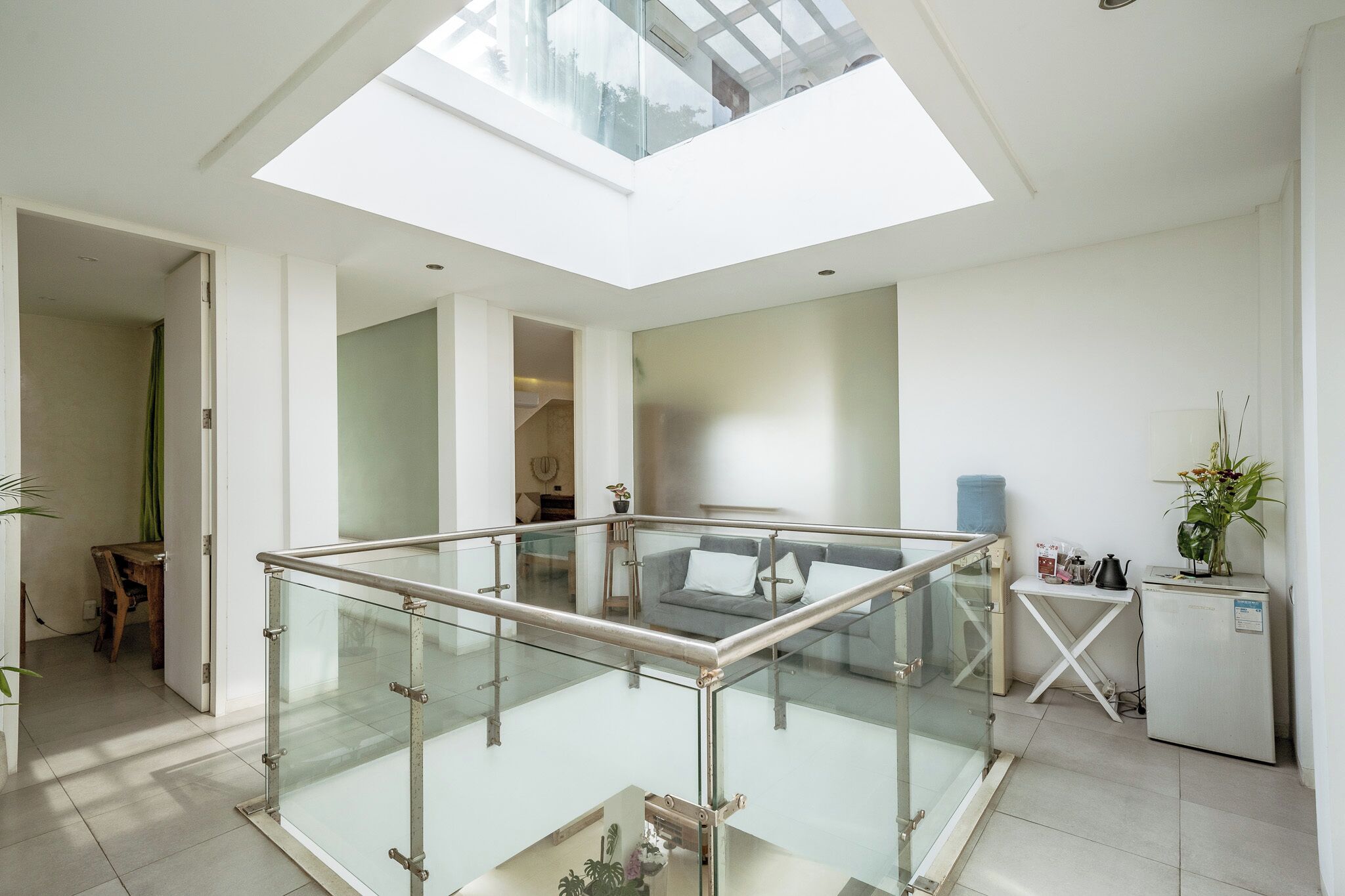 A spacious living area with a glass railing, a sofa, a small table, and a refrigerator.
