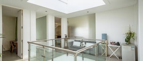 A spacious living area with a glass railing, a sofa, a small table, and a refrigerator.