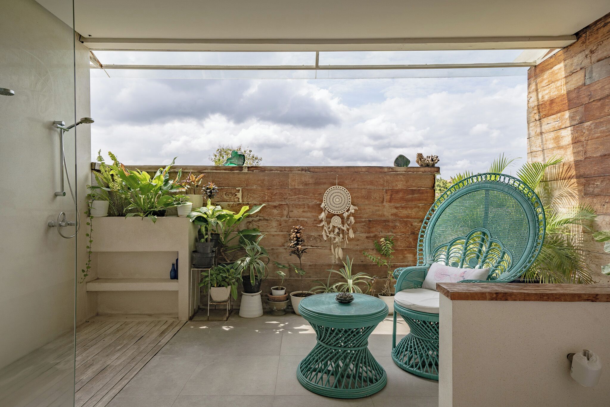 A balcony with a wooden wall, potted plants, and wicker furniture.
