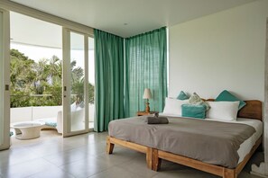 A bedroom with a wooden bed, a nightstand, a lamp, and a view of greenery through a sliding glass door. - Holistic Horizon Bali (Kerobokan)