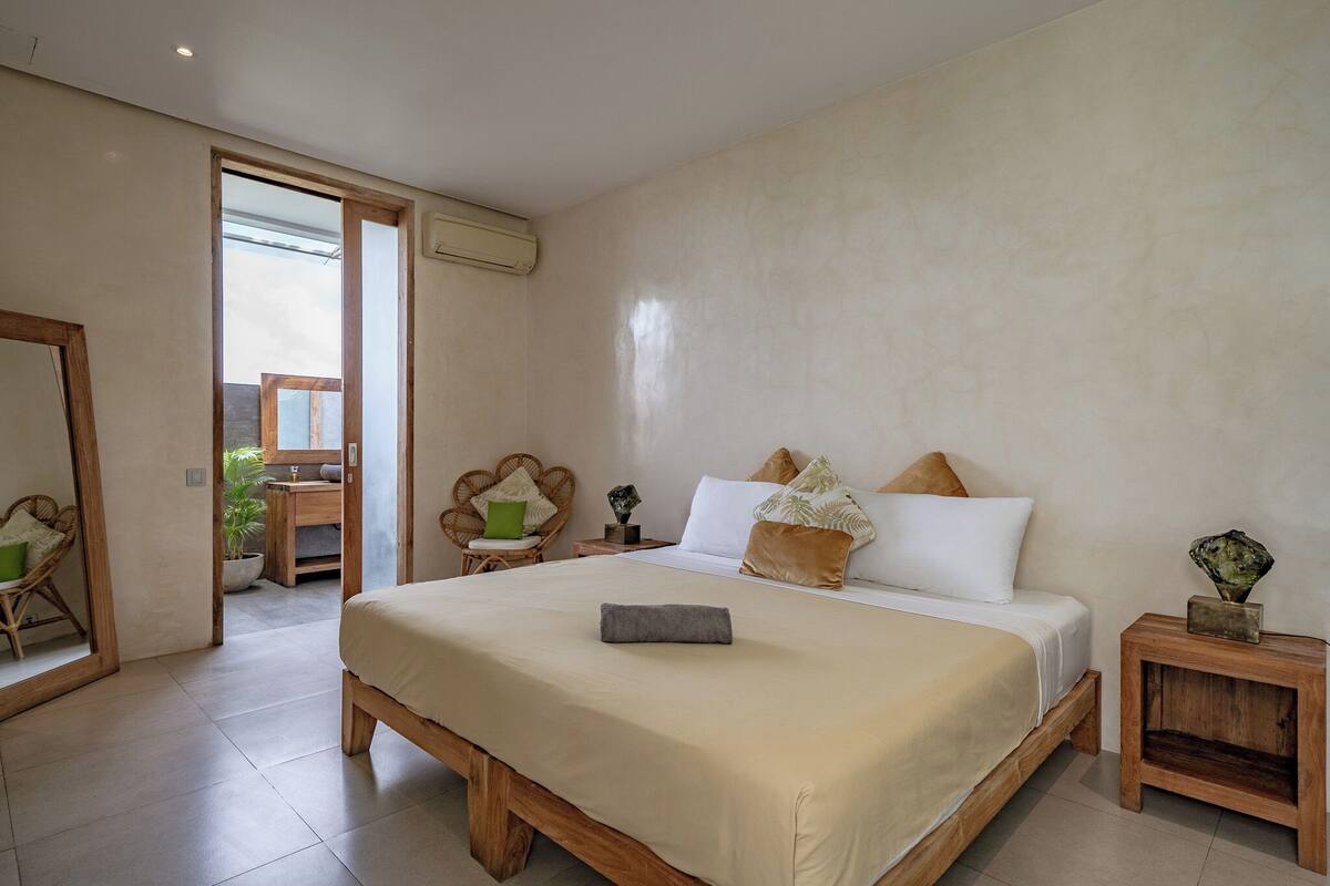 A spacious bedroom with a large bed, wooden nightstands, and a view through an open door.