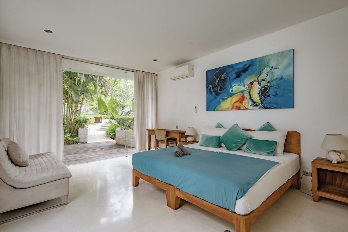 A bedroom with a bed, a chair, a table, and a painting on the wall.