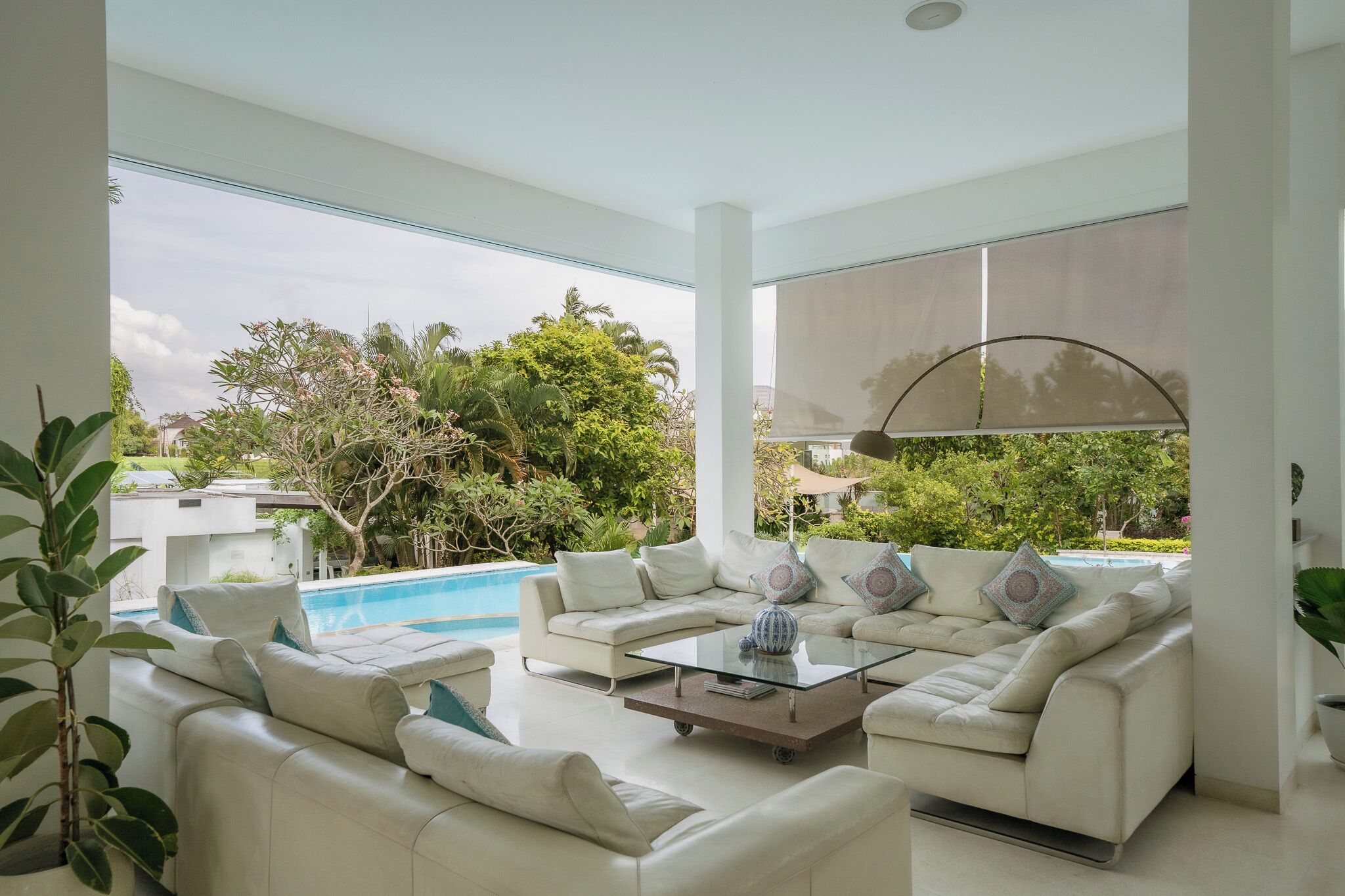 Un salon moderne avec une piscine, des meubles blancs et de grandes fenêtres donnant sur un jardin luxuriant.