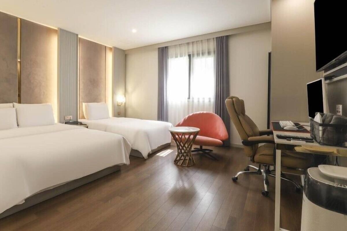 Habitación de hotel con dos camas, un escritorio con computadora, una silla y un televisor.