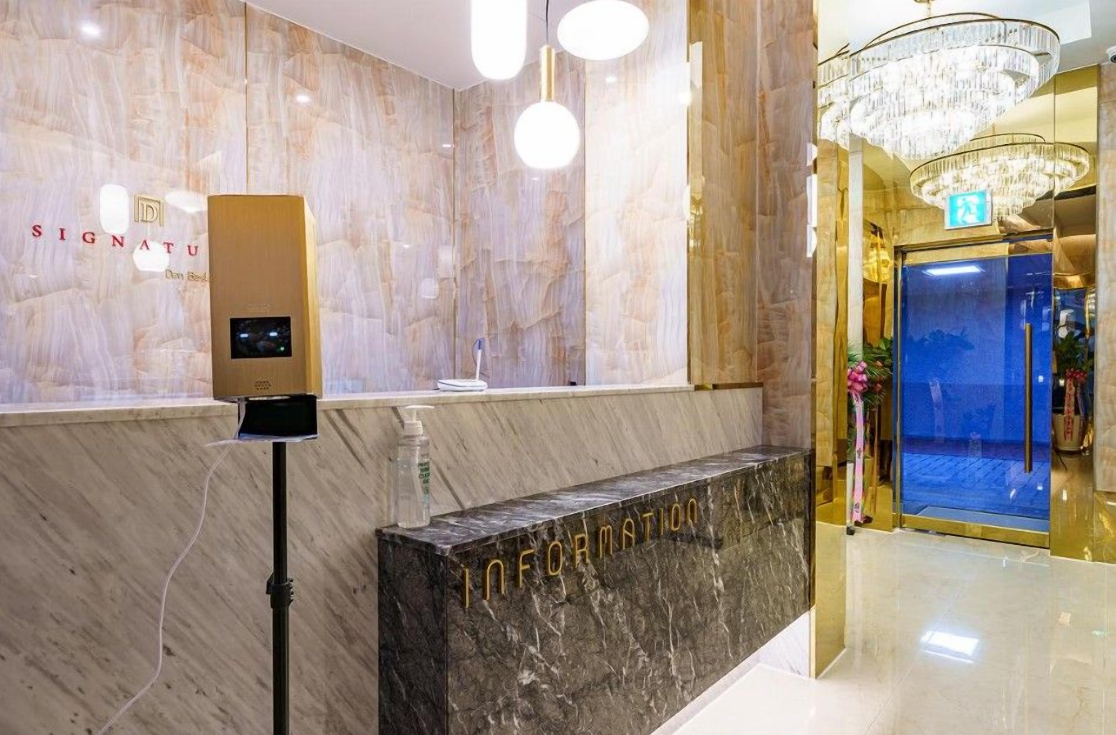 Zona de recepción de hotel con pared de mármol, un quiosco de información digital y una araña de cristal.
