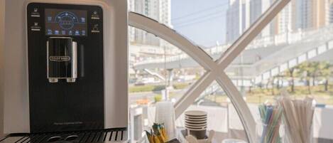 A water dispenser with a digital interface, a tray with napkins, and a window view of a cityscape.