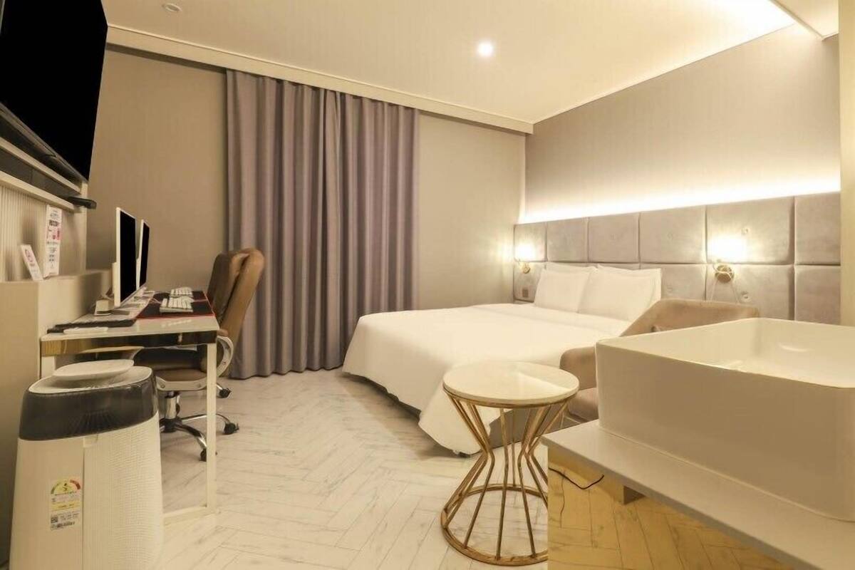 Habitación de hotel con cama, escritorio con computadoras, una silla, una mesa redonda y una bañera.