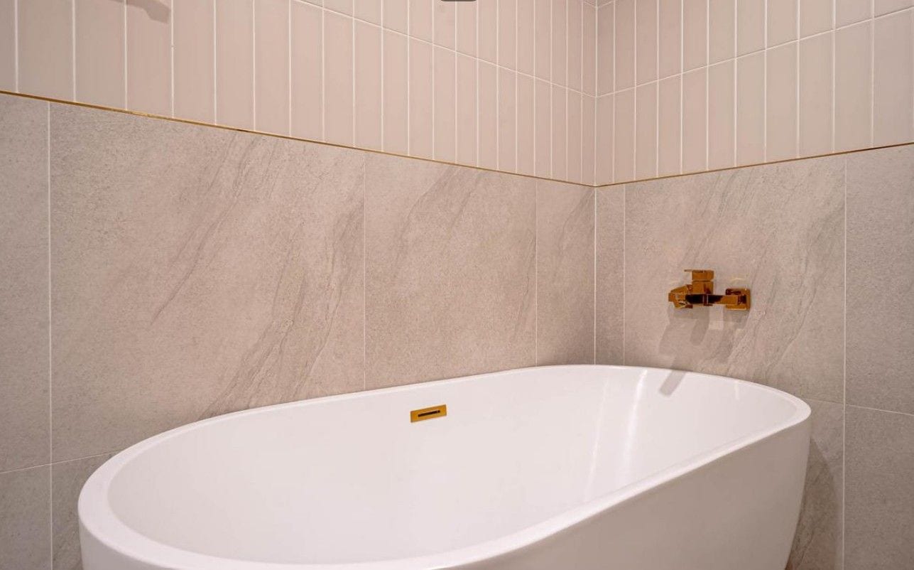 A modern bathroom with a freestanding bathtub, a gold faucet, and a marble wall.