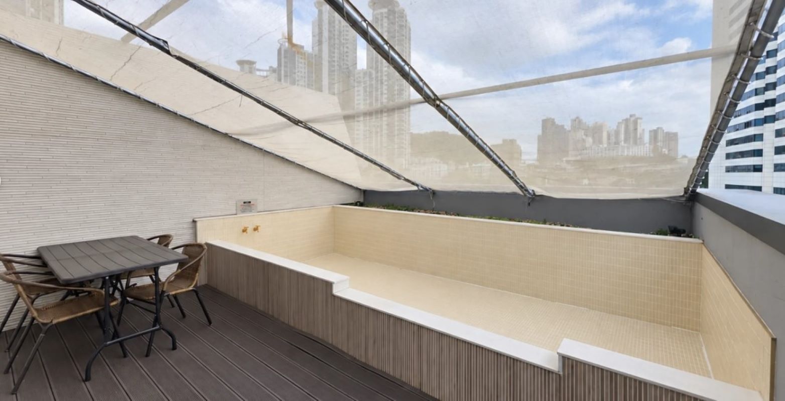 A rooftop terrace with a table and chairs, a small seating area, and a view of a cityscape.